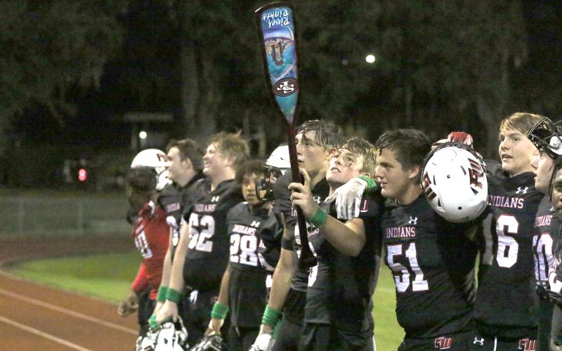 Fort White quarterback Clayton Philpot holds the ‘Paddle’ aloft as the Indians celebrate their win against Santa Fe on Friday night. (MORGAN MCMULLEN/Lake City Reporter)