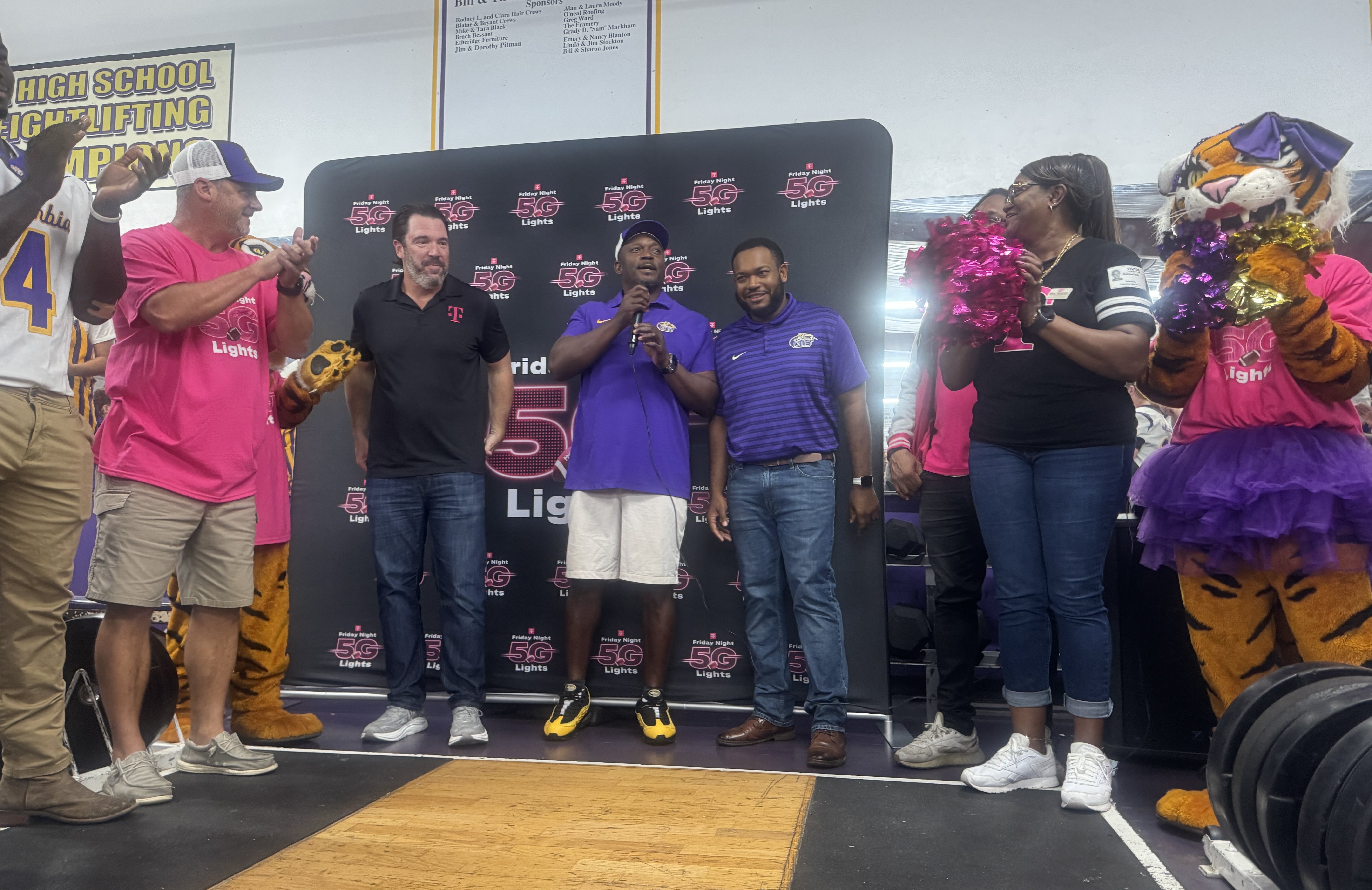Columbia coach Brian Allen (middle) speaks alongside a T-Mobile representative (left) and Columbia offensive line coach Anthony Newton (right) while surrounded by players, staff and cheerleaders as the football program is presented with $25,000 after advancing to the final 40 in the T-Mobile Friday Night 5G Lights competition on Thursday. CHS is now in the running for a $250,000 prize. (JAMIE WACHTER/Lake City Reporter)