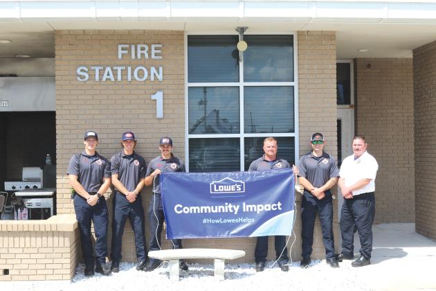 Lake City firefighters Sam Watkins (from left), Nick Chesser, Jerney Morgan, Daniel Dohrn, Gavin McAllister and Lt. Robert Oliver hold a banner promoting the Lowe’s grant that is funding future renovations of the Lake City Fire Department living quarters. (TONY BRITT/Lake City Reporter)