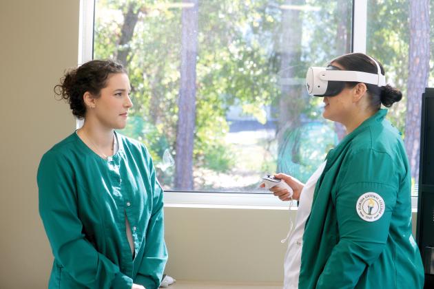 Florida Gateway College nursing student Heather Bellot (left) looks at fellow student Mallory Bedenbaugh as Bedenbaugh utilizes an Occulus virtual reality headset for a training session. (TONY BRITT/Lake City Reporter)