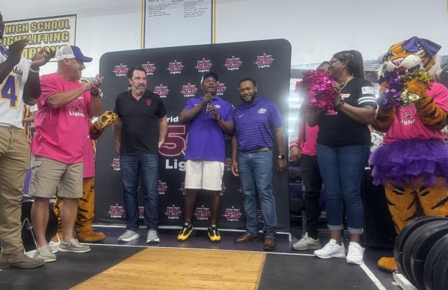 Columbia coach Brian Allen (middle) speaks alongside a T-Mobile representative (left) and Columbia offensive line coach Anthony Newton (right) while surrounded by players, staff and cheerleaders as the football program is presented with $25,000 after advancing to the final 40 in the T-Mobile Friday Night 5G Lights competition on Thursday. CHS is now in the running for a $250,000 prize. (JAMIE WACHTER/Lake City Reporter)