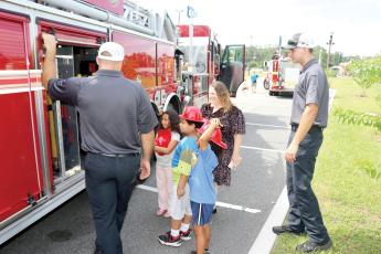 Lake City Fire Department firefighter Chase Hancock (from left) lets Ryker Paris, 7, Jeremiah Williamson, 7, Ariella Paris, 7 and Melissa Angeles look at the equipment firefighters use on emergency calls during the Firefighters and Cones event. (TONY BRITT/Lake City Reporter)