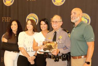 Florida Highway Patrol Troop B District Commander Mike Burroughs holds a service weapon in a box that was a presented to him as a retirement present as he is pictured with members of his family Friday. (TONY BRITT/Lake City Reporter)