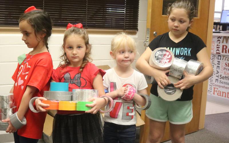 Eastside Elementary School students Ryleigh Trespalacios (from left), Aunna Hartopp, Summer Bedenbaugh and Ariana French bring rolls of duct tape to the school library Thursday morning. The school hopes to set a world record for the largest ball of tape. (TONY BRITT/Lake City Reporter)