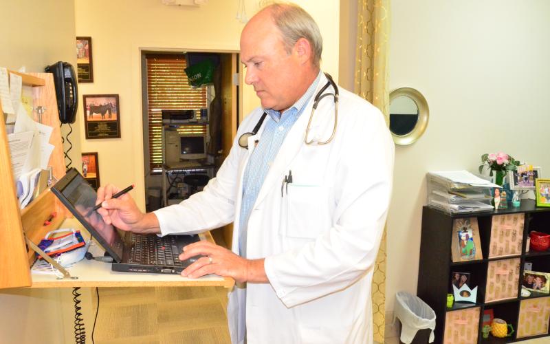 Local physician Peter Giebeig, who practices family medicine, performs administrative work at a computer station in his practice. Giebeig says the pandemic has cut business in half due to patients being more cautious about where they go in public. (CARL MCKINNEY/Lake City Reporter)