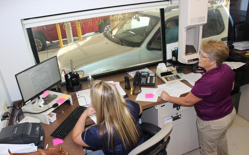 Columbia County Tax Collector’s Office customer service representatives Miranda Lee, left, and Annette LeMay assist customers in the drive-through lanes at the courthouse annex office Wednesday afternoon. The tax collector’s office has been closed to foot traffic since March 26, but continues to assist customers with limited transactions in the drive-through. (TODD WILSON/Lake City Reporter)