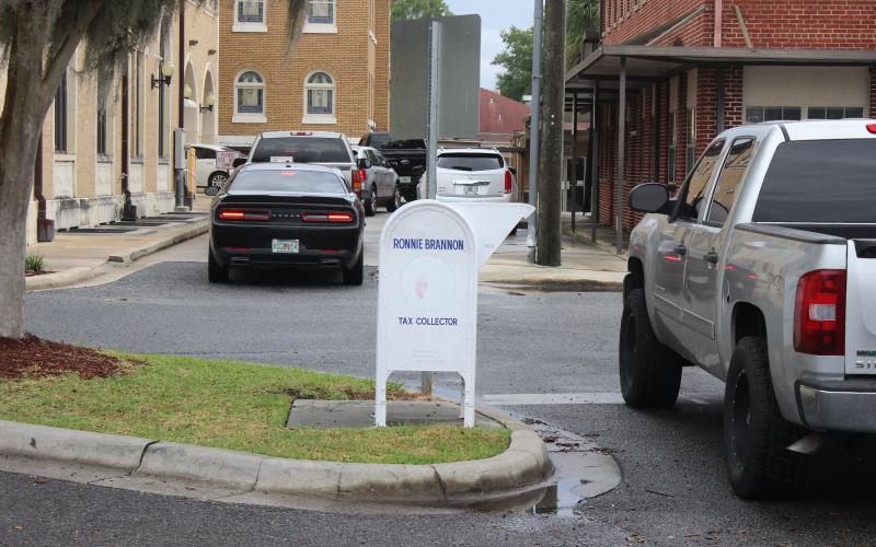 Vehicles wait in line to enter the two lanes of the drive-through at the Columbia County Tax Collectors office Monday afternoon. Property owners also may drop their tax payment checks in the white drop box, center, or call and pay by phone with a credit card or pay online at: www.columbiataxcollector.com. (TODD WILSON/Lake City Reporter)
