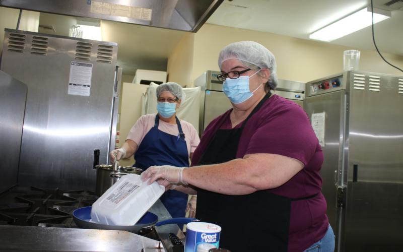 Felecity Houghton (foreground) opens a pack of hamburger while Cindy Brannon stirs a pot of vegetables. (TONY BRITT/Lake City Reporter)
