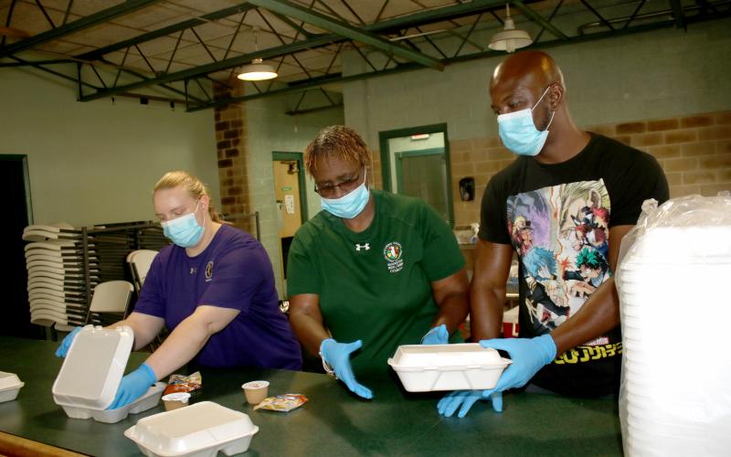 Columbia County Recreation Department employees Courtney Rowe (from left), Lynda Caldwell and Chad Owens practice preparing and distributing meals in the Richardson Community Center cafeteria Thursday afternoon. (TONY BRITT/Lake City Reporter)