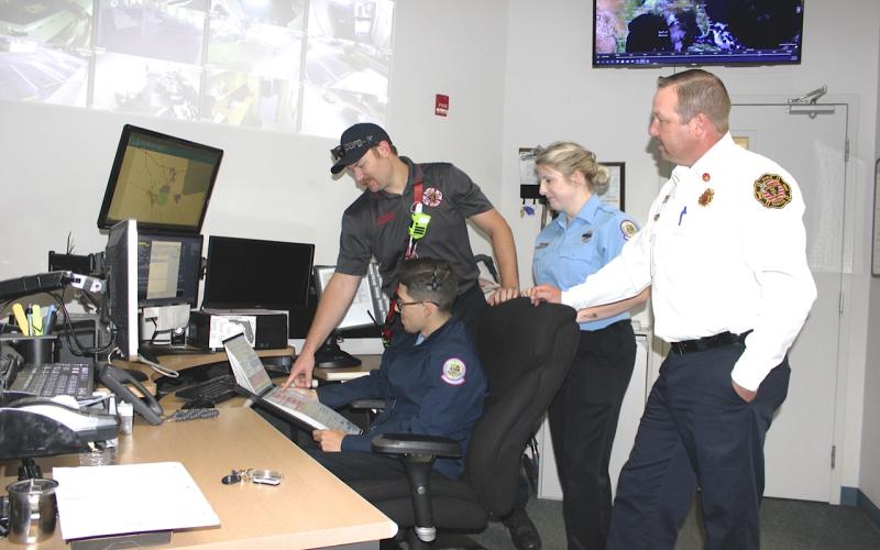 Dispatcher Marcel Ferro (seated) uses a backup code book to explain the Lake City Fire Department’s new Fire Priority Dispatch System that went online Wednesday. Firefighter Matt Herndon, (left) Communication Supervisor Megan Hollis and LCFD Assistant Chief Joshua Wehinger look on. The new fire and rescue dispatch system trains dispatchers on how to gather more pertinent information from 911 callers quickly and pass it along to responding fire and rescue first responders. (TODD WILSON/Lake City Reporter)