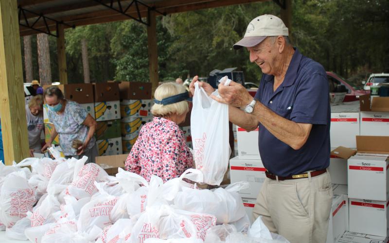 Bud Parker works on tying a plastic bag as he and other volunteers at Lake City Church of Christ distribute food and other commodities Thursday afternoon. More than 200 vehicles passed through the event collecting bags and boxes of food. (TONY BRITT/Lake City Reporter)