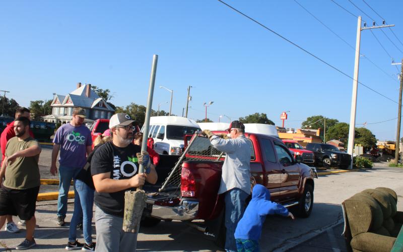 Chip Parker carries a pole to a trash dumpster, while other volunteers unload a truck, during Saturday’s Clean Lake City event. (TONY BRITT/Lake City Reporter)