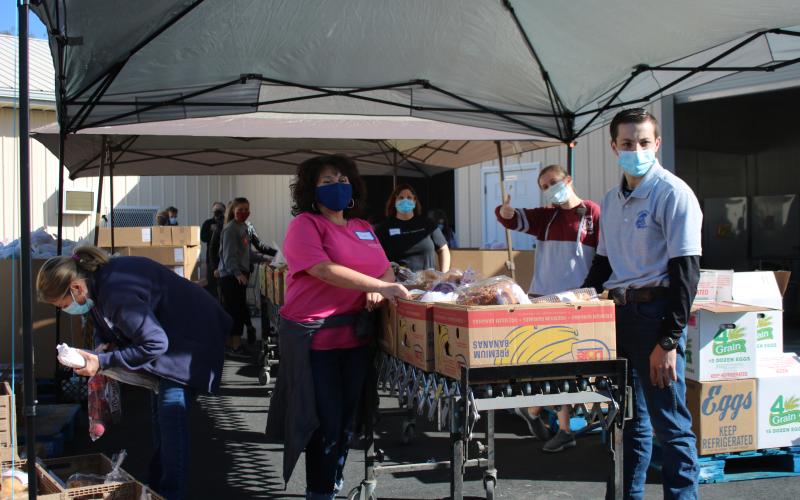 Tina Seifert (left) stands with Josh Eadie, a student volunteer, as they wait to push boxes of food down a conveyor belt as Catholic Charities clients get their Thanksgiving baskets on Thursday. (TONY BRITT/Lake City Reporter)