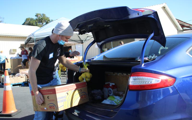 Jared Fraze, a Covenant Community School student, puts bags of food into a client’s car during Thursday’s Catholic Charities Thanksgiving basket giveaway. (TONY BRITT/Lake City Reporter)