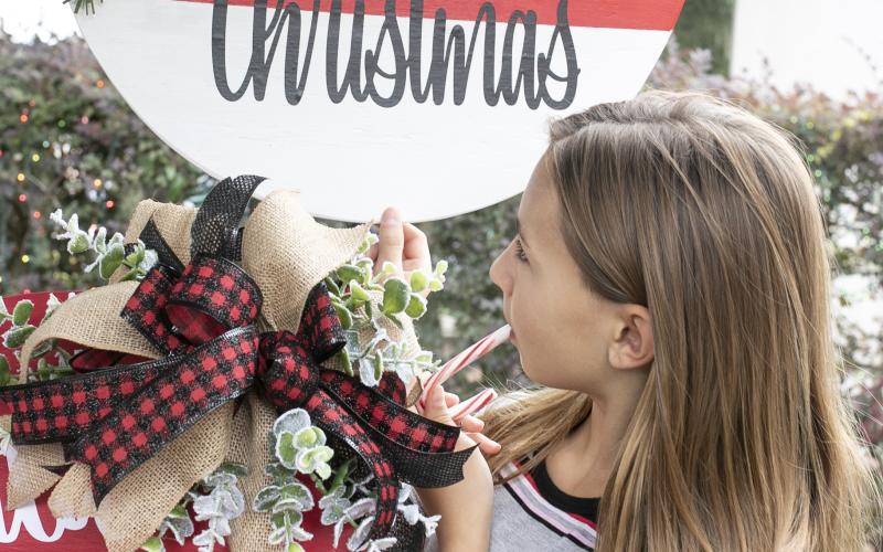 Aubree Craig, 10, of Lake City enjoys a candy cane as she looks through decorative door hanger signs at the P.S. We’re Crafty Door Hanger booth at the Holiday Market craft festival Saturday. (JEN CHASTEEN/Special to the Reporter)
