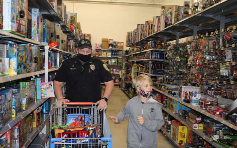 Lake City Police Department Officer Michael Craig looks at a shopping cart full of items as Wyatt Russo looks at more toys for potential Christmas gifts. (TONY BRITT/Lake City Reporter)