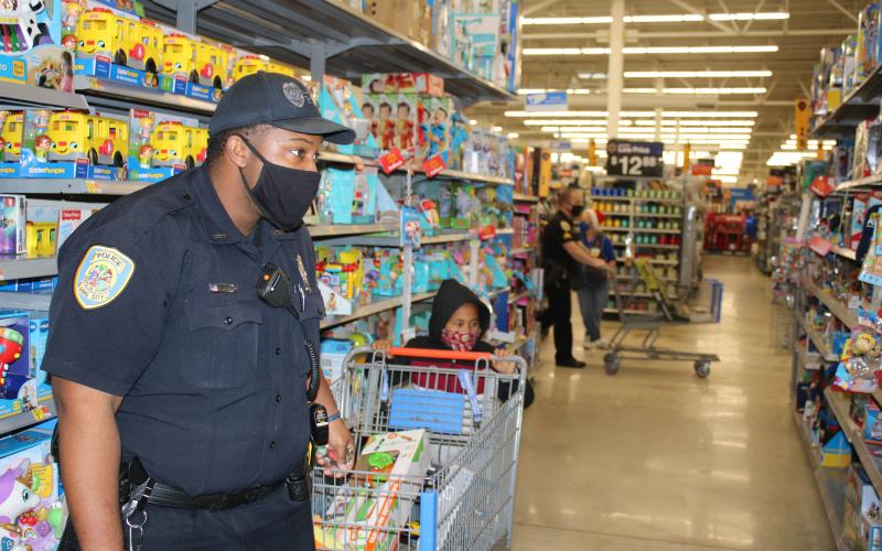 Lake City Police Officer Tyrone Sheppard casts an intent look at prices as he helps a child look for Christmas gifts Wednesday. (TONY BRITT/Lake City Reporter)