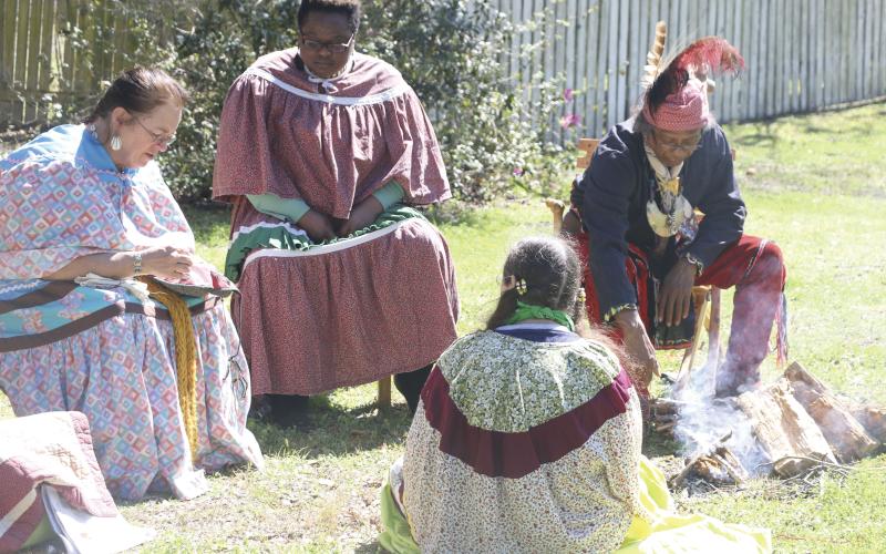 A volunteer in Seminole attire tends a fire as others join in knitting garments. (MORGAN MCMULLEN/Lake City Reporter)