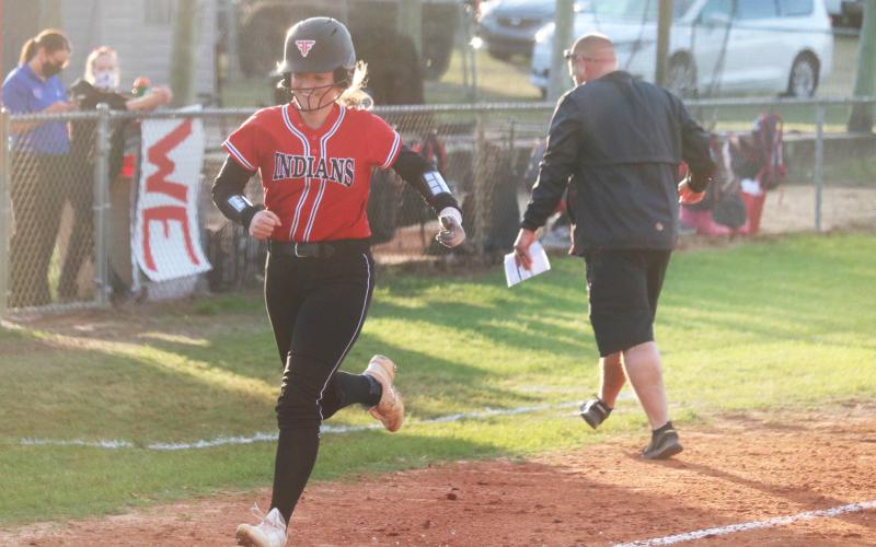 Fort White’s Kadence Compton smiles heading toward home plate after hitting a home run against Bronson while assistant coach Chad Padgett celebrates on Friday night. (JORDAN KROEGER/Lake City Reporter)