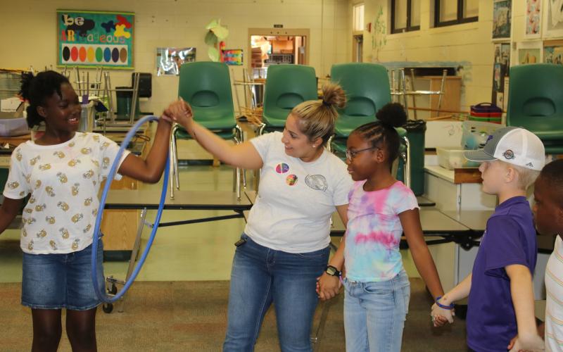 An unidentified child is passed a hula hoop from Columbia County Sheriff’s Office School Resource Deputy Nicole Martell during an activity during camp Tuesday. (TONY BRITT/Lake City Reporter)