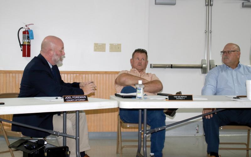 County Attorney Joel Foreman, left, reads the county charter off his phone Thursday after officials were informed their meetings in Fort White may be in violation. County Commissioners Tim Murphy, center, and Rocky Ford listen. (TONY BRITT/Lake City Reporter)