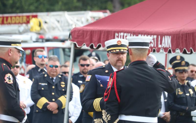 Lake City Assistant Fire Chief Josh Wehinger is presented the American flag that was draped across Fire Chief Randy Burnham’s casket during the graveside ceremony Friday. (TONY BRITT/Lake City Reporter)