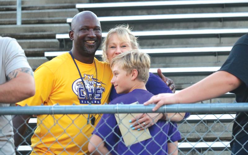 Columbia High School football head coach Demetric Jackson (left) hugs Crystal and Fisher Hair Wednesday afternoon at Tiger Stadium at a memorial service for Skipper Hair. (JORDAN KROEGER/Lake City Reporter)