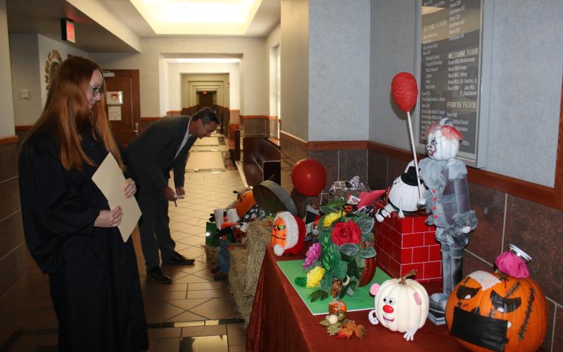 Several decorated pumpkins, including one that resembles Pennywise the Dancing Clown from the movie ‘It,’ sit in the lobby of the Columbia County Courthouse as Columbia County Judge Sara Carter (left) and Columbia County Clerk of Courts Jay Swisher examine entries. (TONY BRITT/Lake City Reporter)