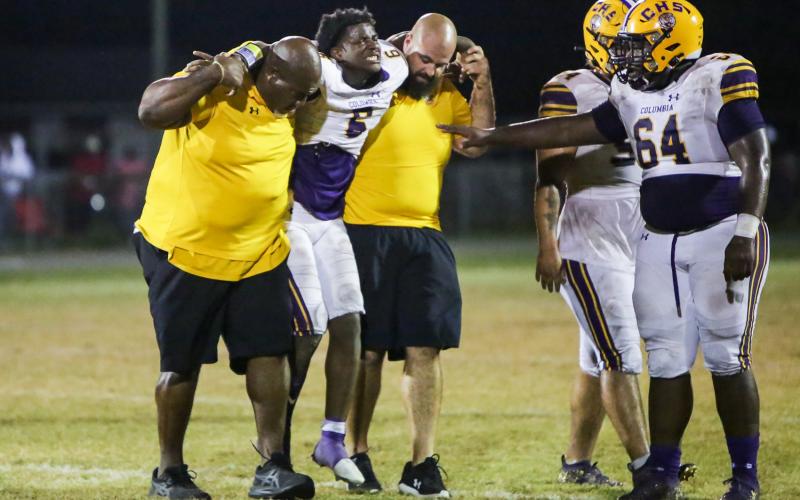 Columbia’s Tray Tolliver is helped off the field by defensive line coach Mark Campbell and co-defensive coordinator John Woodley during last Friday’s game against Madison County. (BRENT KUYKENDALL/Lake City Reporter)