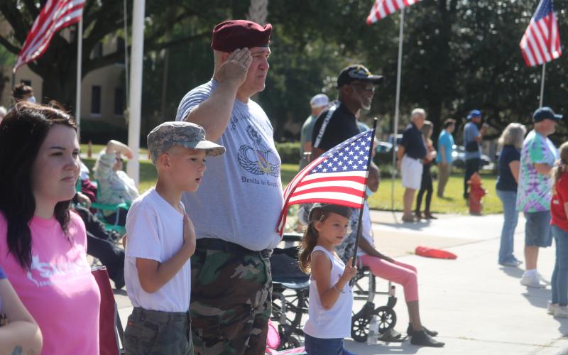 Liam Ambrose (from left), 10, U.S. Army veteran Harrison Ambrose and Bailee Ambrose, 7, stand as the Columbia High School band plays the National Anthem during Thursday’s Veterans Day parade in Lake City. (TONY BRITT/Lake City Reporter)