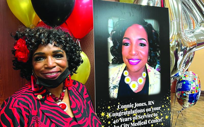 Connie Jones smiles next to a sign honoring her 40 years working at Lake City Medical Center. (COURTESY)