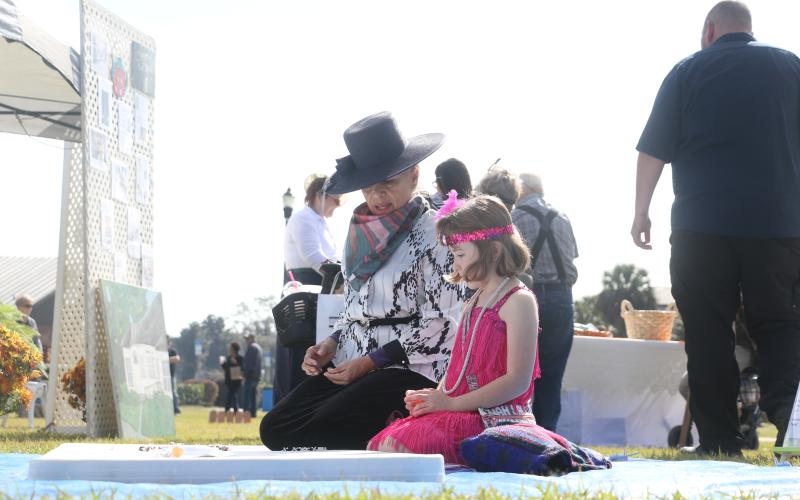 Dulcinea Strube (left) teaches 7-year-old Olivia Carr how to play jacks near the Woman’s Club setup Saturday during Founder’s Day celebrations. (MORGAN MCMULLEN/Lake City Reporter)
