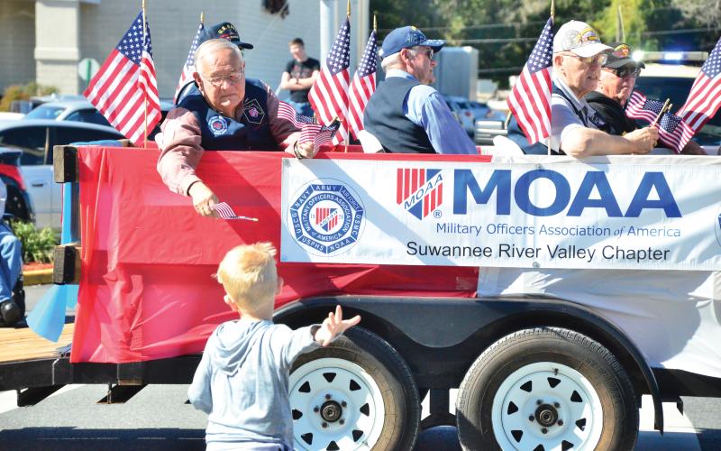 A member of the Military Officers Association of America hands a flag to a child during the 2019 Veterans Day Parade in Lake City. (FILE)
