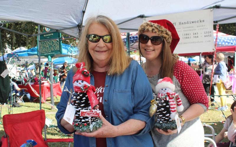 Janice Medford (left) and Jaime Brock show off snowmen made out of pinecones at a vendor’s booth on Saturday. (TONY BRITT/Lake City Reporter)