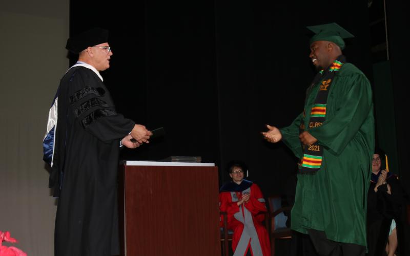 A Florida Gateway College graduate walks across the stage Friday during a commencement ceremony to receive his degree from Brian Dopson, the college’s vice president of academic affairs. FGC hosted the first two of four graduation ceremonies Friday, the other two are scheduled for Monday. (TONY BRITT/Lake City Reporter)