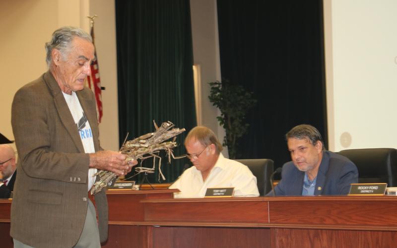 Tom Cunilio (from left), representing the Center of Sustainable Agroforestry, provides Columbia County commissioners Robby Hollingsworth and Toby Witt, with samples during Thursday’s night’s commission meeting as he requested funding for a a field day showcasing energy crops. (TONY BRITT/Lake City Reporter)