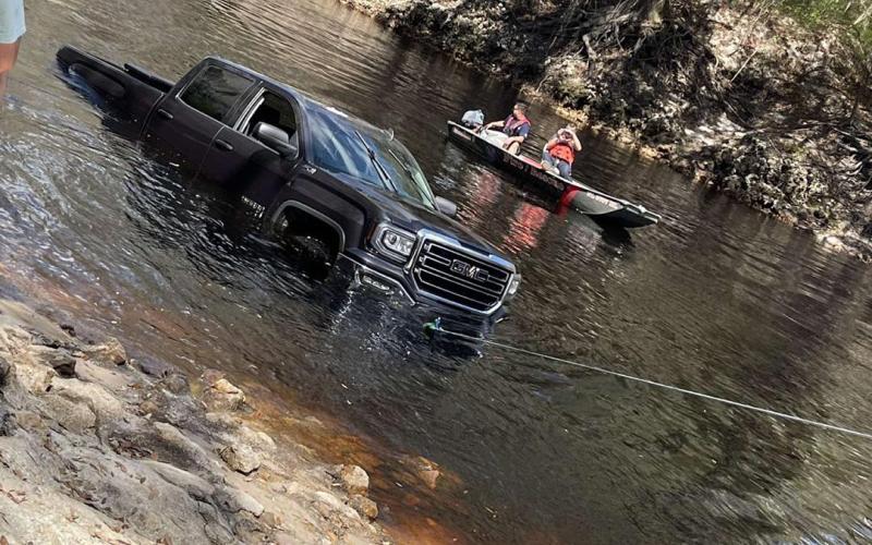 A black GMC truck gets a tow out of the Suwannee River Saturday afternoon after it rolled into the water. (COURTESY)
