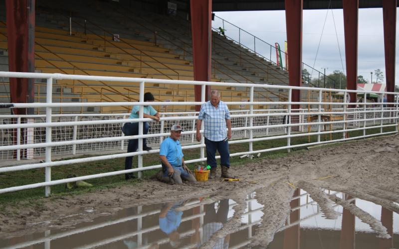 Dale Brown (middle) and Terry Hayes get muddy while working on verifying stakes that will be used for timers during the 28th Aannual Florida Gateway Pro Rodeo in the Florida Gateway Fairgrounds Rodeo Arena on Thursday afternoon. Kylee Brown (left) looks on. (TONY BRITT/Lake City Reporter)