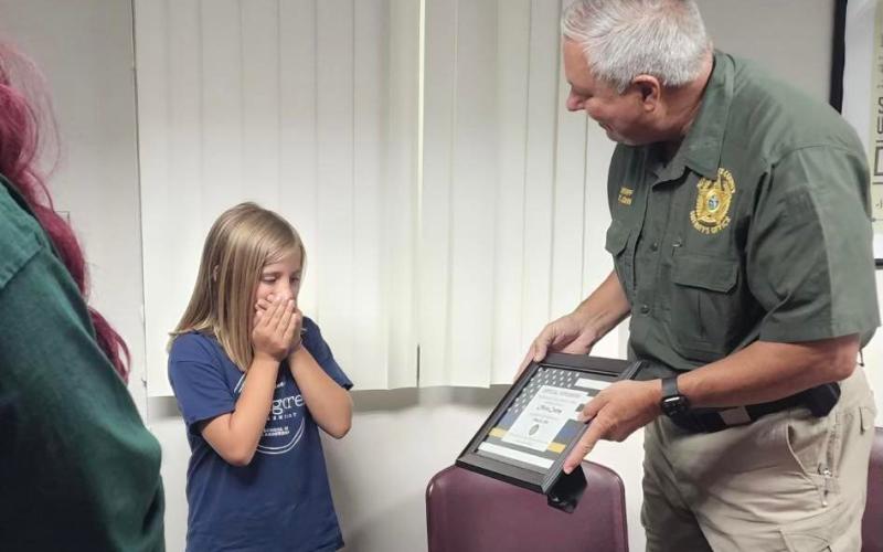 Olivia Cauley, 9, receives an ‘official superhero’ certificate from Suwannee County Sheriff Sam St. John on Tuesday for her actions on May 14 to assist her mother, Stephanie, following a medical emergency. (COURTESY)