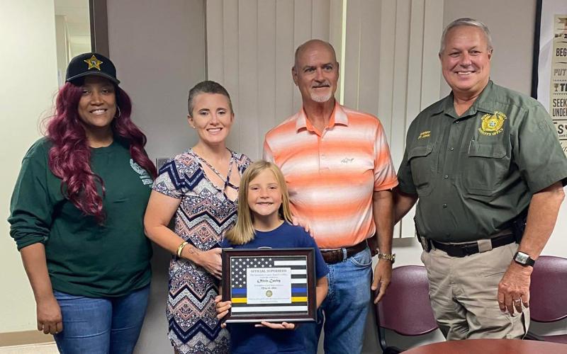 Olivia Cauley is pictured with Suwannee County Dispatcher Cheryl Gross-Tillman, her parents Stephanie Cauley and Donnie Harrison and Sheriff Sam St. John after receiving her certificate declaring her an 'official superhero.' (COURTESY).