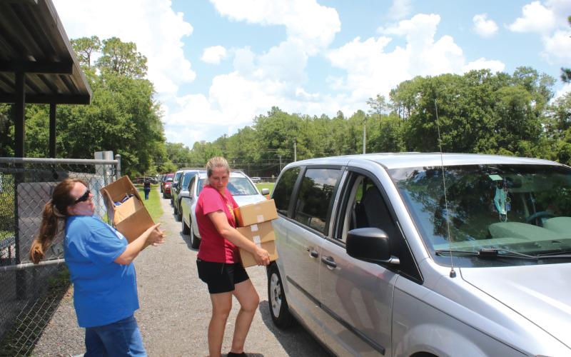 Alicia Blackford (from left) and Laurie Renegar carry meals to a minivan at Five Points Elementary School last summer. (FILE)