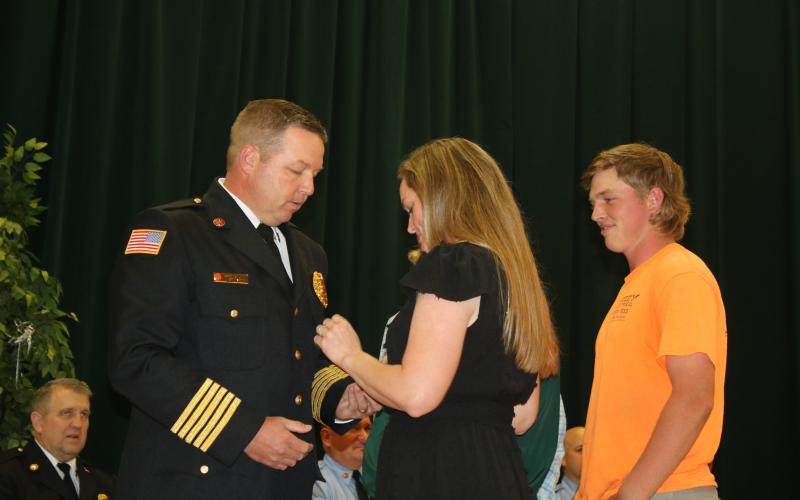 Lake City Fire Chief Josh Wehinger receives his badge from wife, Lari, as son, Ty, looks on during a swearing-in ceremony Tuesday night at the Columbia County School District Administrative Complex Auditorium. (TONY BRITT/Lake City Reporter)