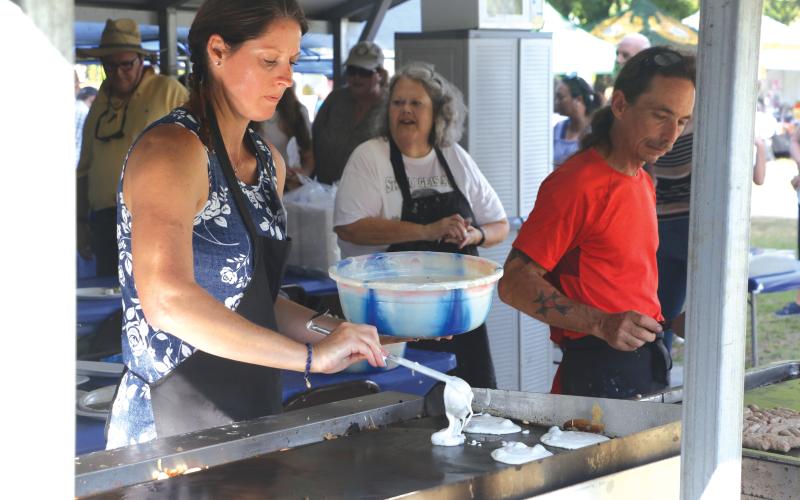 Volunteer Jennifer Petit puts fresh blueberry pancake batter on the griddle during the blueberry pancake breakfast at last year’s Wellborn Blueberry Festival. (FILE)