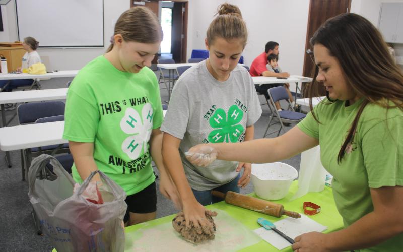 Elizabeth Davis (from left), 16, and Wren Wilkerson, 13, 4H Four Paws members get baking tips and help from Candice Green as the teens work on creating animal treats for dogs on Saturday. (TONY BRITT/Lake City Reporter)