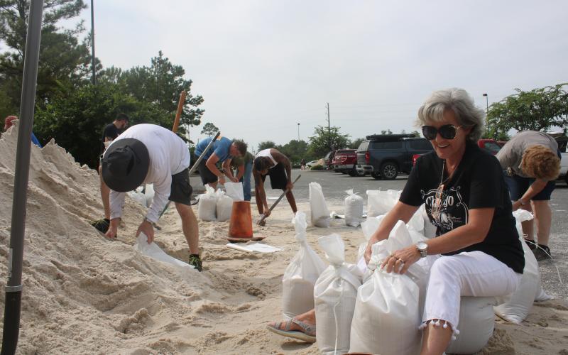 Lila Pasternak sits on sandbags in the Southside Sports Complex on Tuesday morning while tying other sandbags. The county public works department placed several piles of sand in the parking lot allowing residents to fill the bags or get aid from others at the site, which will be open from 7 a.m.-7 p.m. today. (TONY BRITT/Lake City Reporter)