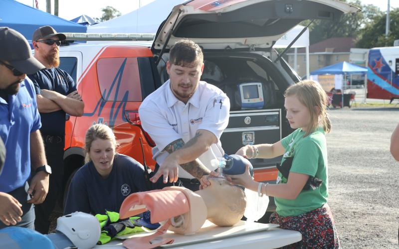 Jadyn Simpson (right) learns how to work a pump resuscitation bag at a Century Ambulance booth Tuesday night during the Lake City Police Department’s National Night Out event. (MORGAN MCMULLEN/Lake City Reporter)