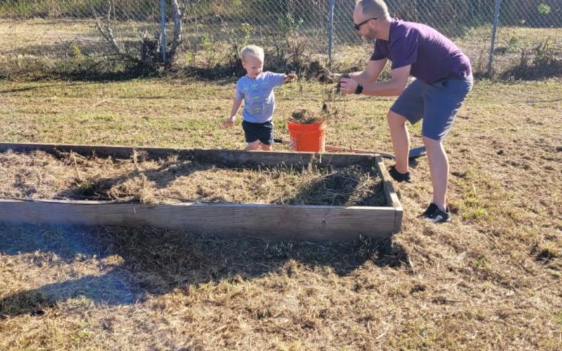 A volunteer plays with a child as they work toward building out a raised plant bed at Richardson Community Center Saturday. (COURTESY)