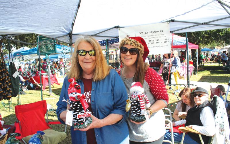 Janice Medford (left) and Jaime Brock show off snowmen made out of pinecones at a vendor’s booth during last year’s holiday market. (FILE)