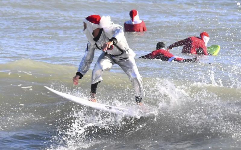 Surfer Corey Howell in a space man Surfing Santa suit, rides with waves with other surfing Santas for the 14th annual Surfing Santas of Cocoa Beach event Christmas Eve morning, Saturday, Dec. 24, 2022. Cold temperatures in the 30s Fahrenheit thinned out the surfers, but thousands showed up for the annual holiday event that benefits the Florida Surf Museum and Grind for Life, a local charity benefiting people with cancer. (MALCOLM DENEMARK/Florida Today via AP)