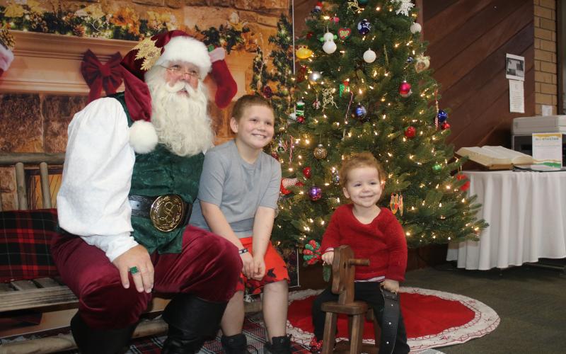 Santa Claus (from left) gets smiles from Bentley Strickland, 9, and Carleigh Holeman, 3, during an after-hours event at the Columbia County Public Library that was attended by more the 25 children. (TONY BRITT/Lake City Reporter)